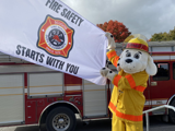 Sparky the Fire Dog holding flag with Scugog Fire logo and words 'Fire Safety Starts With You'