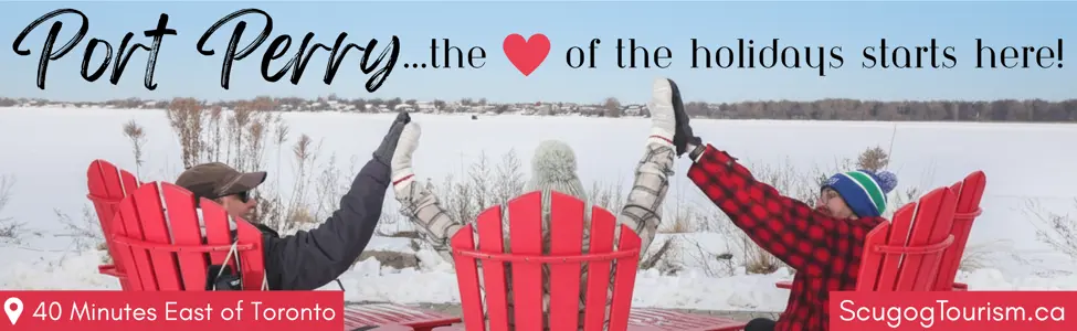 Three people in red Muskoka chairs high fiving while facing frozen lake. Text on top reading 'Port Perry...the heart of the holidays starts here!'. Text boxes in left and right corners reading '40 Minutes East of Toronto' and 'ScugogTourism.ca' respectively