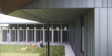 fenced area with caged rooms for animals and man playing with dog on grass