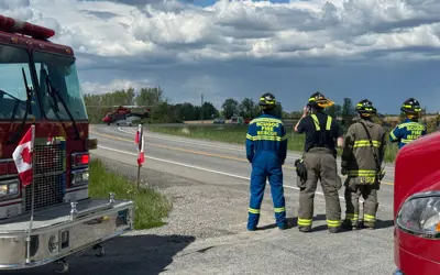 Four firefighters facing away from camera, looking down road at landing helicopter